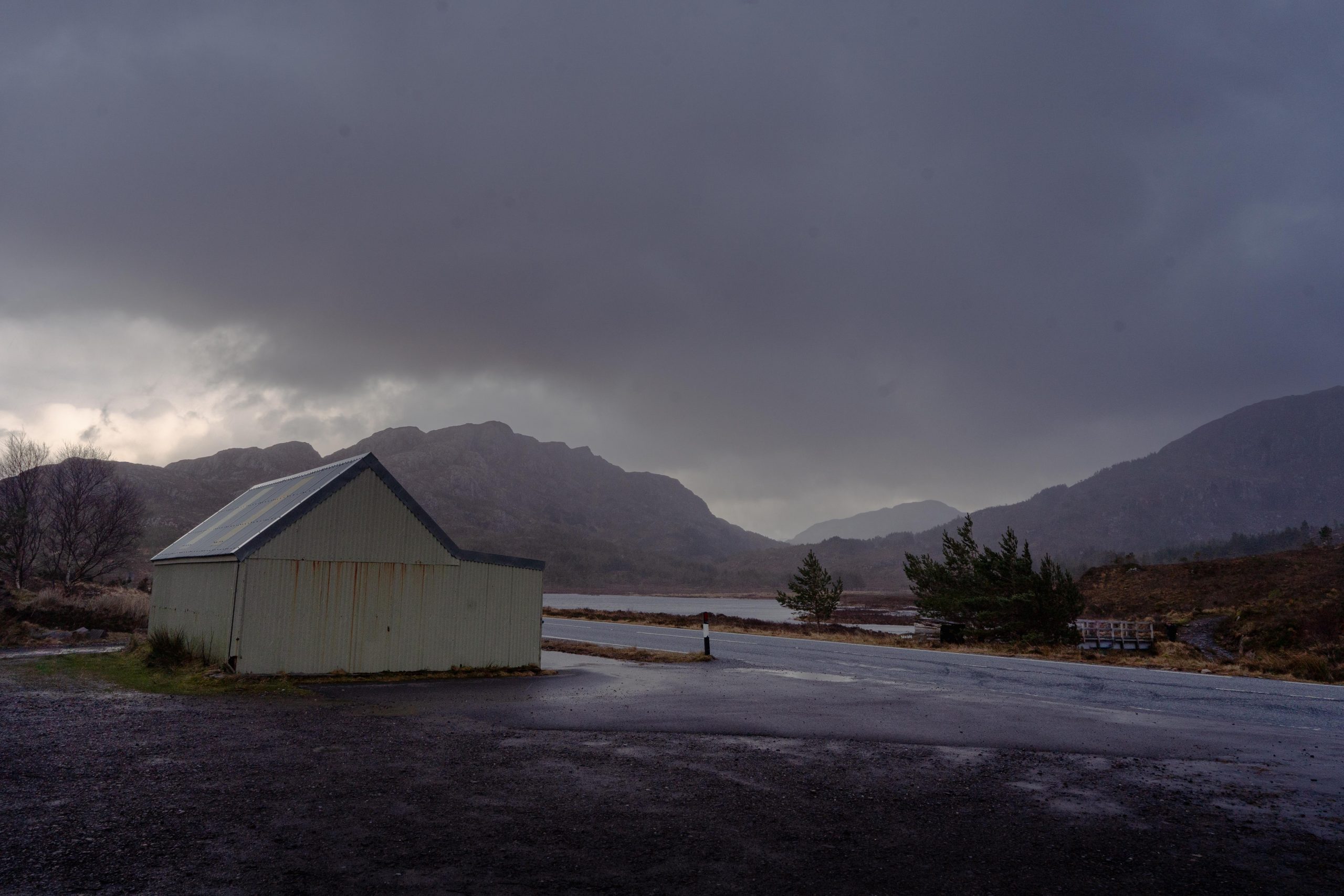 Temporary shelter under a stormy sky surrounded by mountains, hints of red and purple act as lowlights across the image. the shelter over looks Loch Bad an Sgalaig