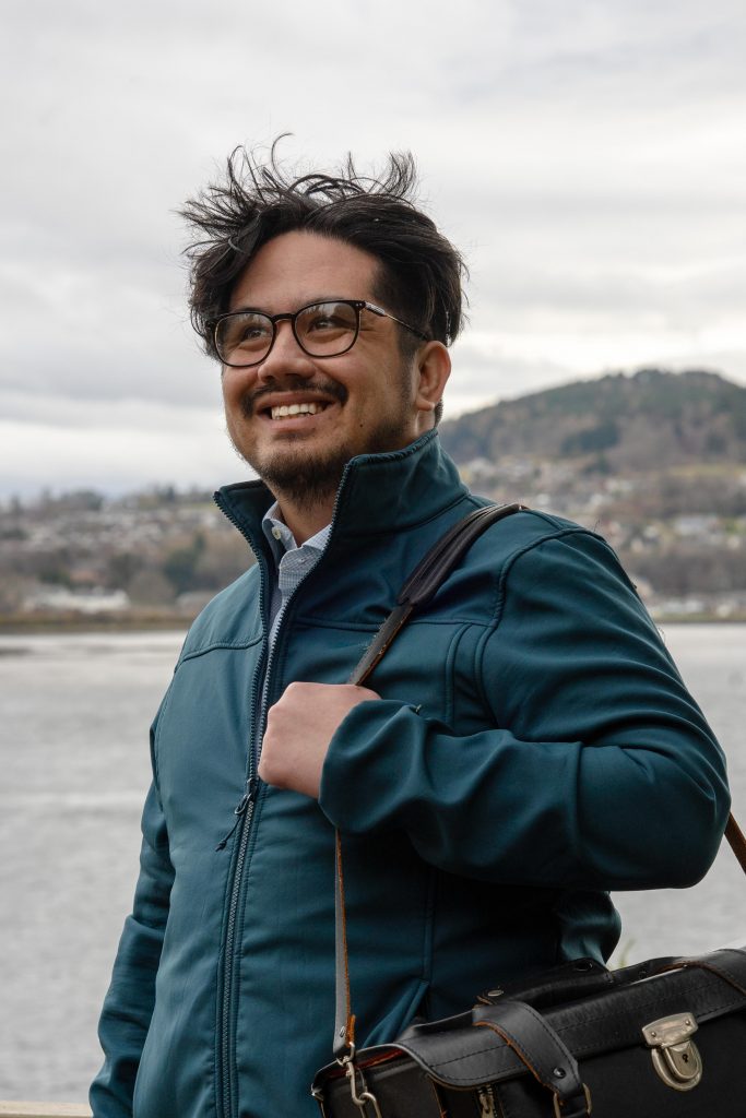 Young Man at the centre of the image holding a leather doctors bag, posed in front of the Beauly Firth shot from North Kessock